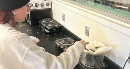 A student uses a stirrer to push undyed wool roving into a pot on the stove containing mordant and water.