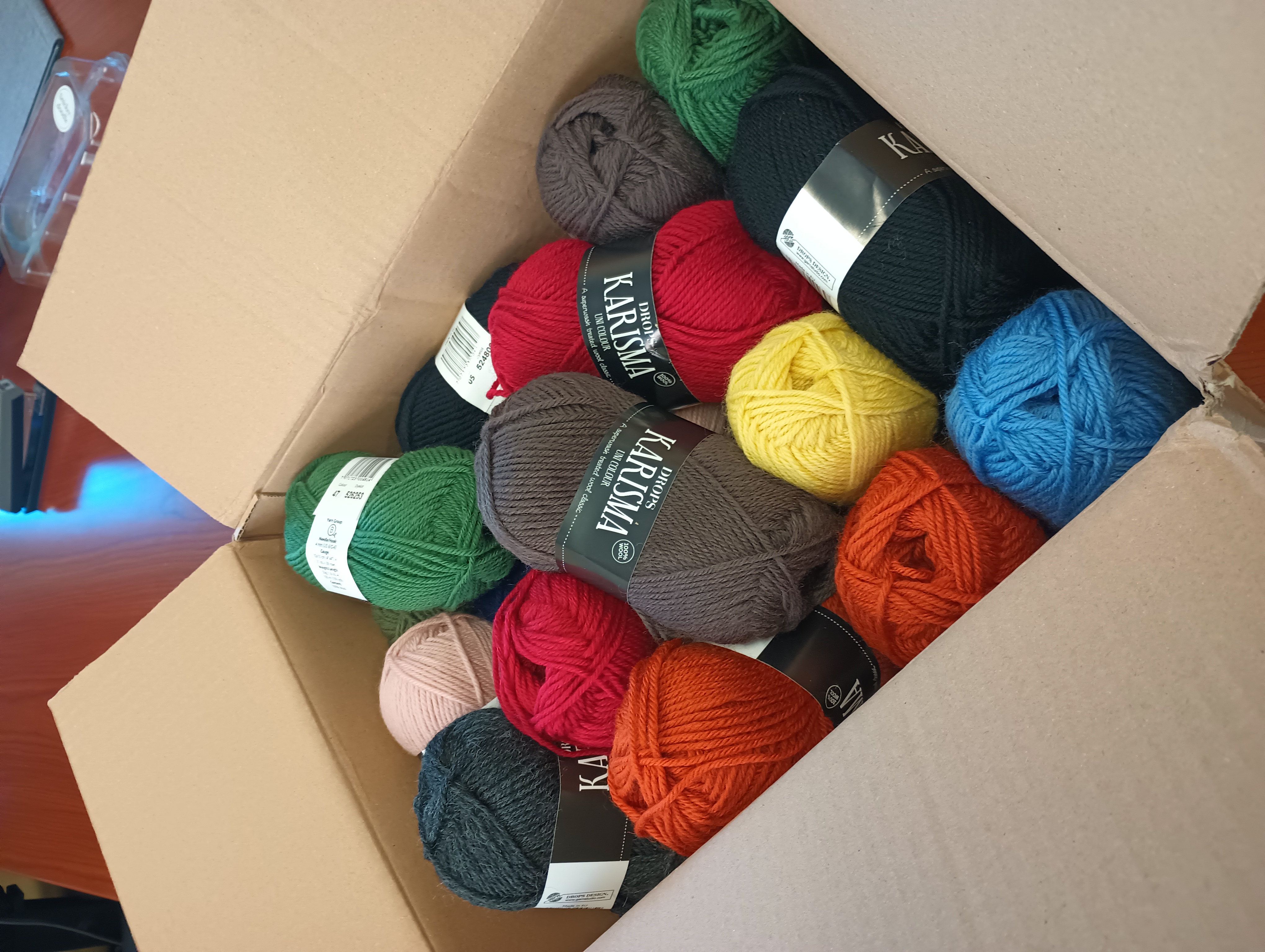 A large box full of skeins of Karisma brand wool yarn in various colors.