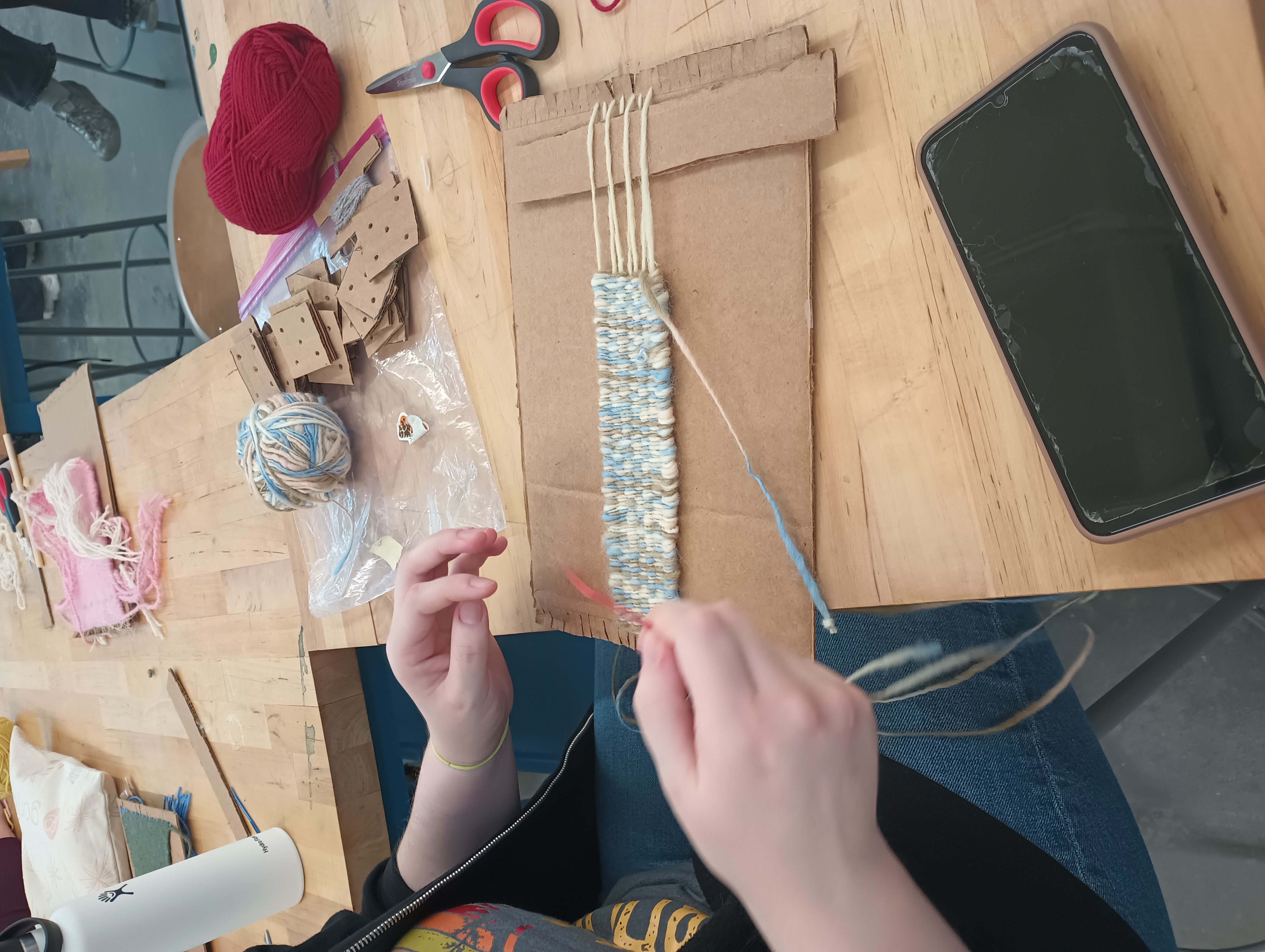 Closeup of a narrow piece on a cardboard loom in speckled pale blue and brown.