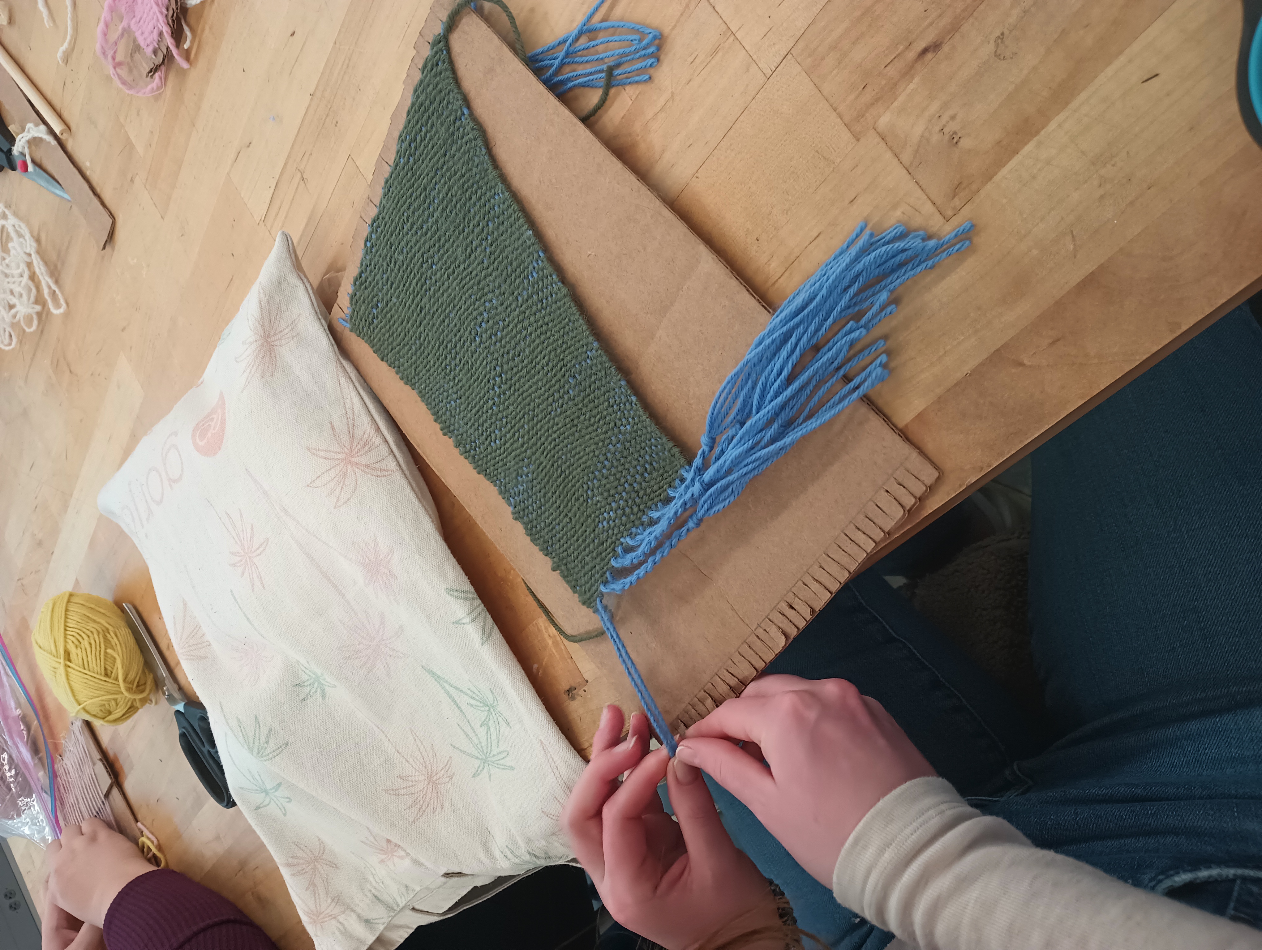 A student twists blue tassels out of the warp of their woven piece.