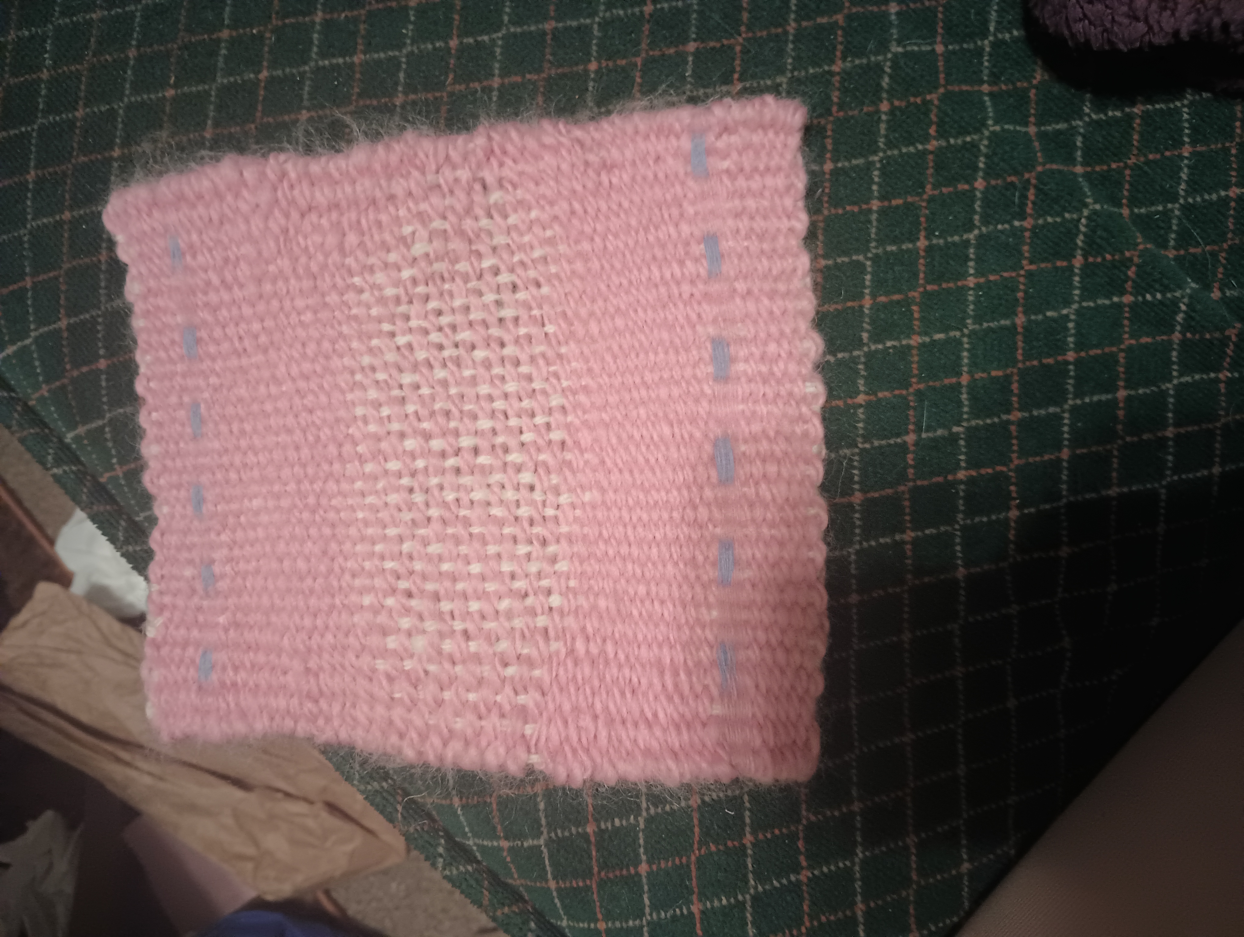 A woven rectangle of white warp, pink weft, and with some blue checks. The tabby weave is quite evident, especially where it is balanced instead of weft-faced.