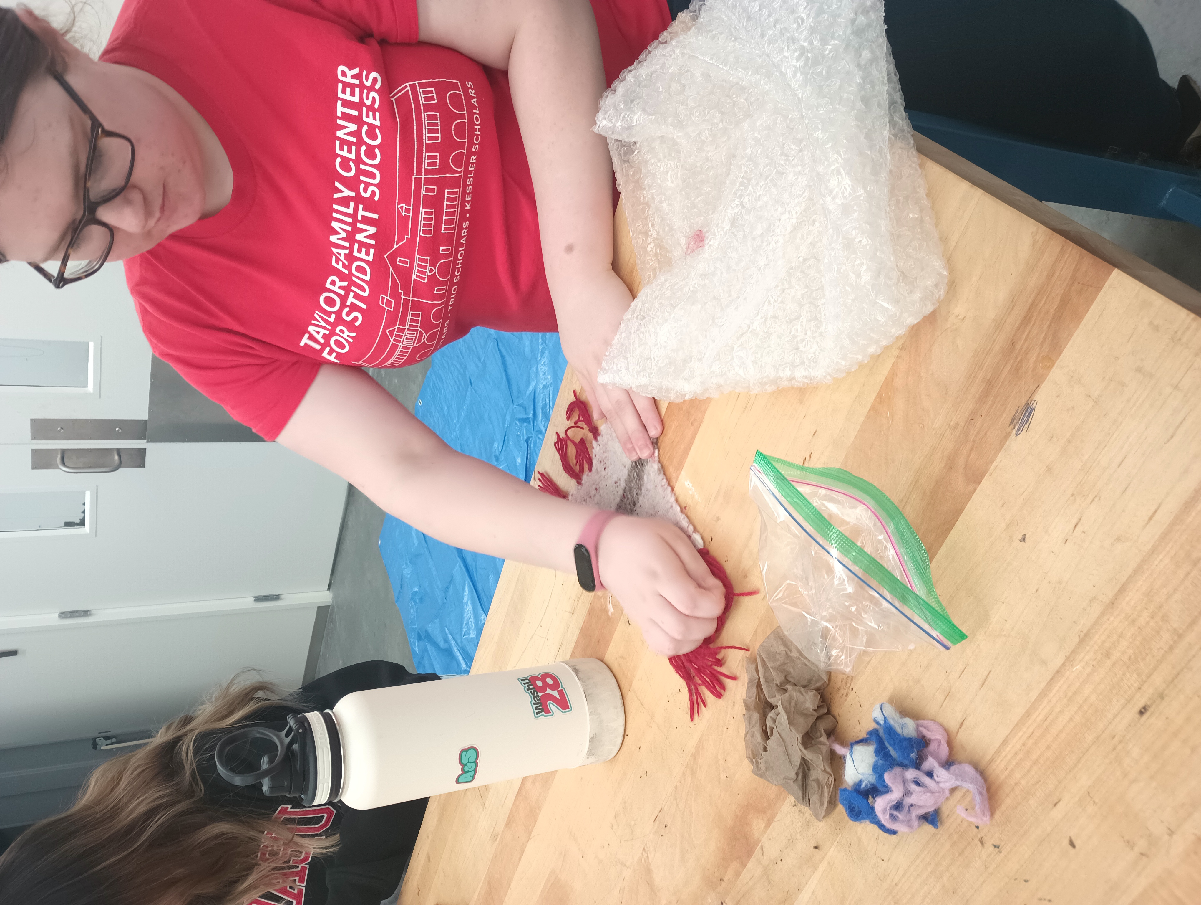 A student applies pressure and friction to a woven wool rectangle with her hands. 