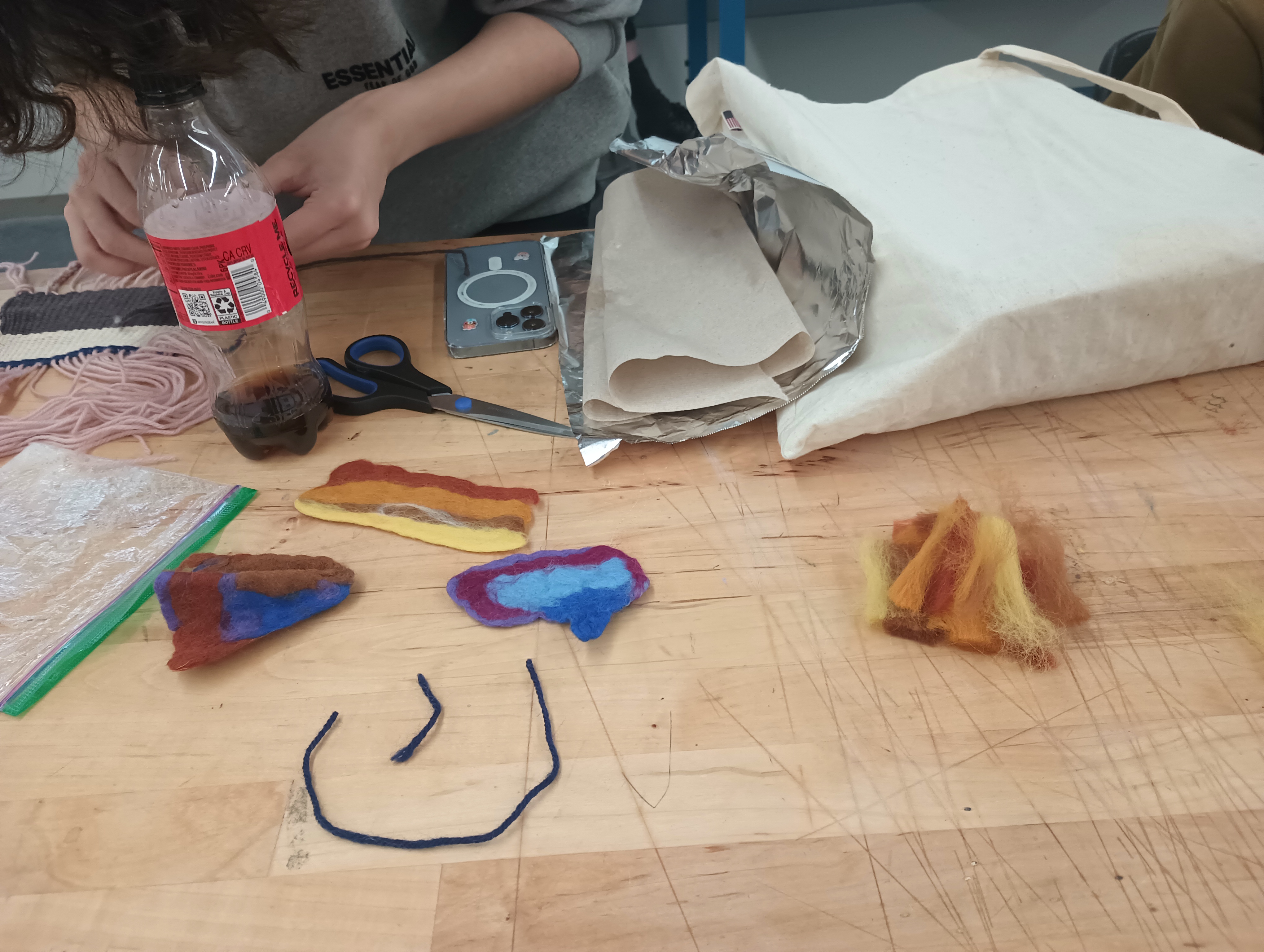 Two pieces of colorful felt arranged on a table above two pieces of yarn forming a smiley face. 