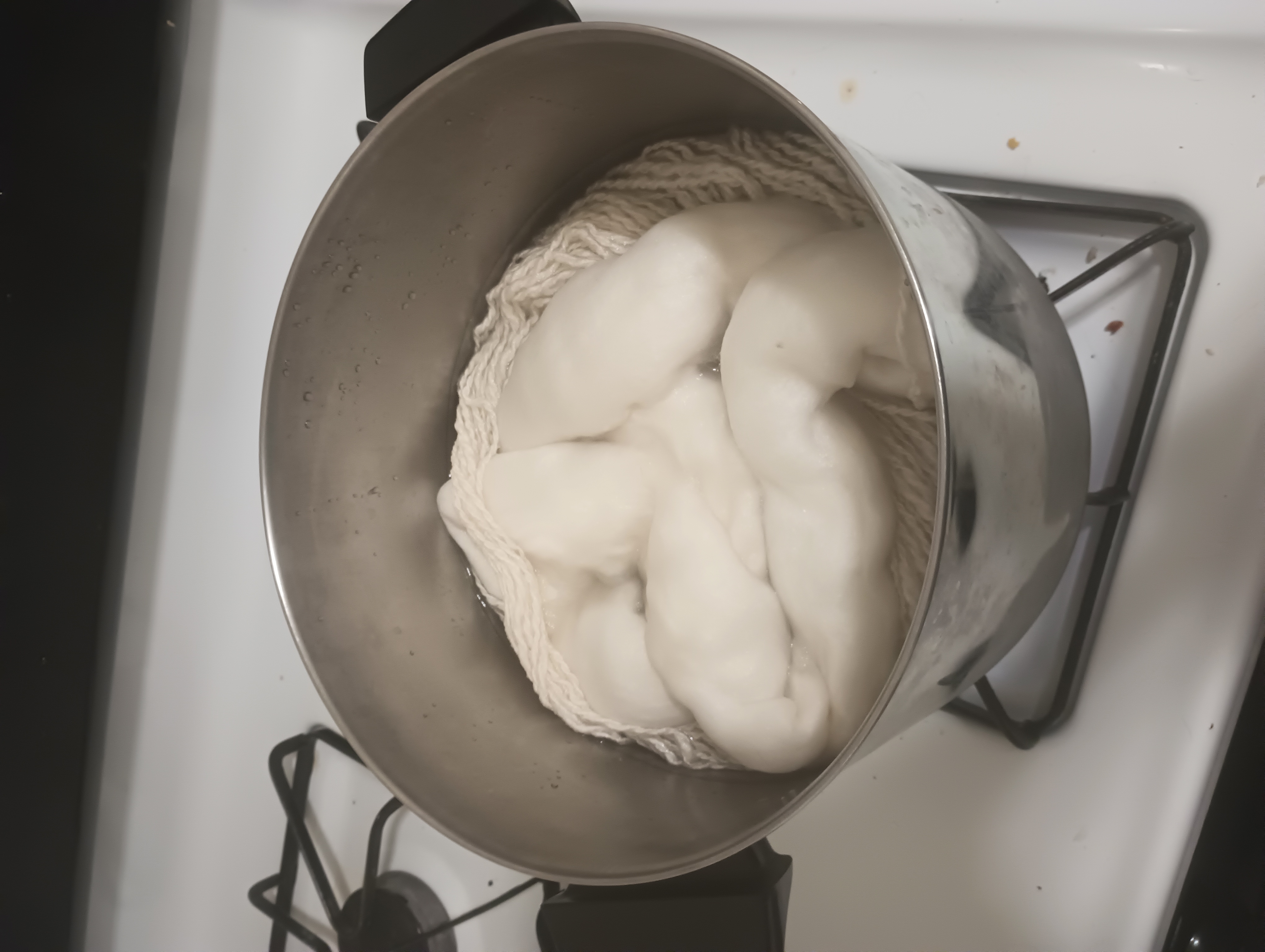 Undyed wool roving and handspun yarn cook in a pot of mordant and water.