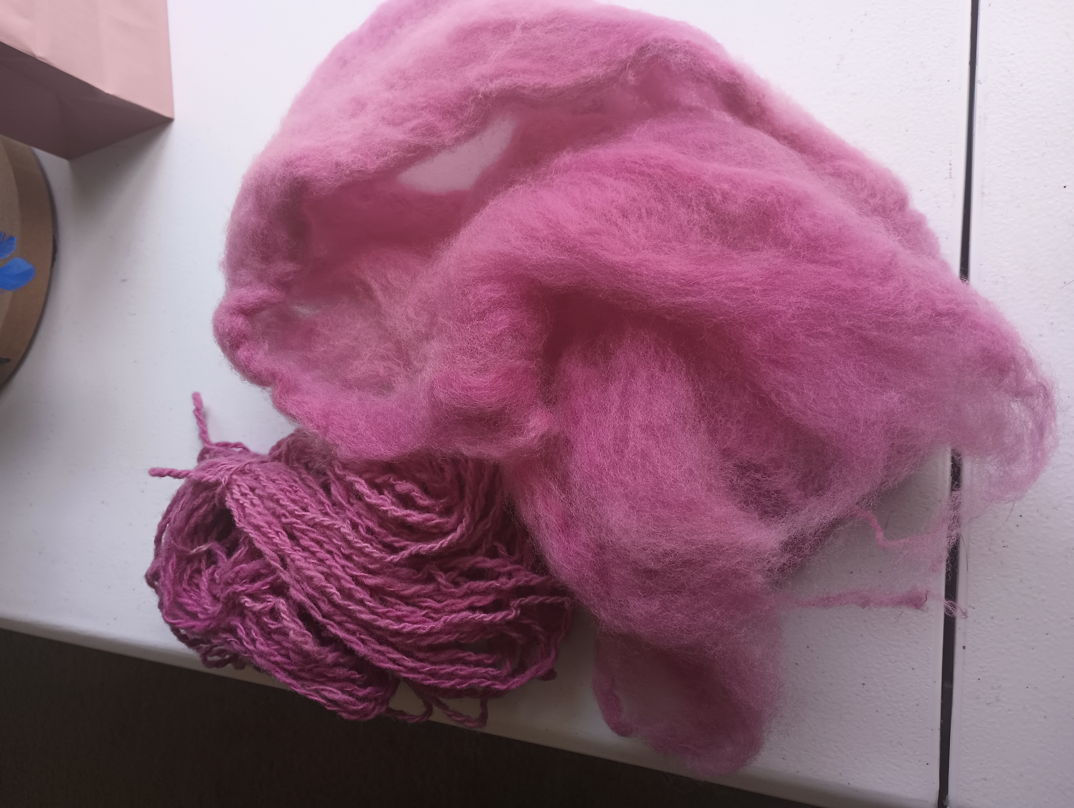 A skein of magenta cochineal-dyed yarn sits next to wool roving dyed the same color.