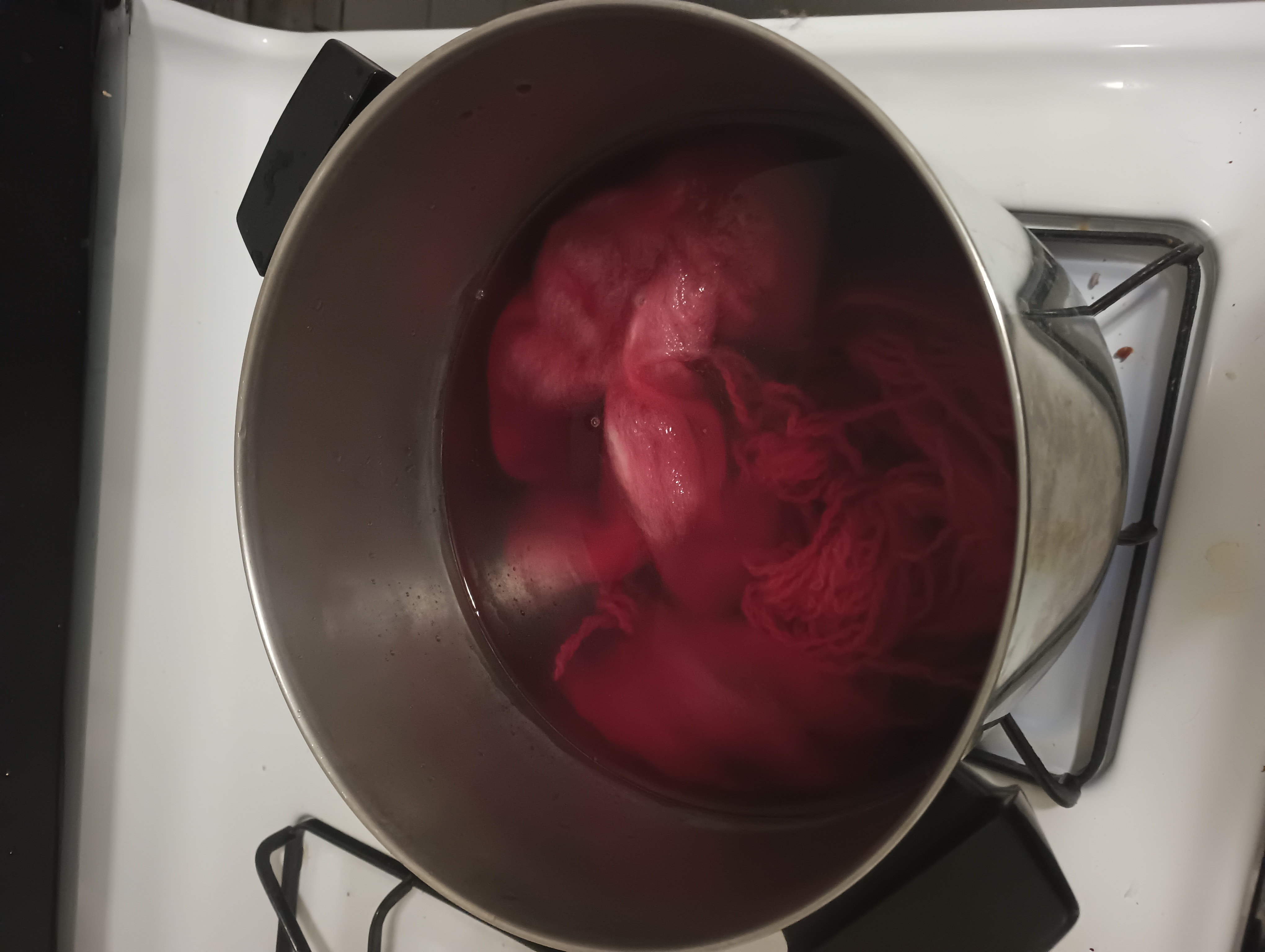 Wool roving and yarn cook in a pot of magenta cochineal dye.
