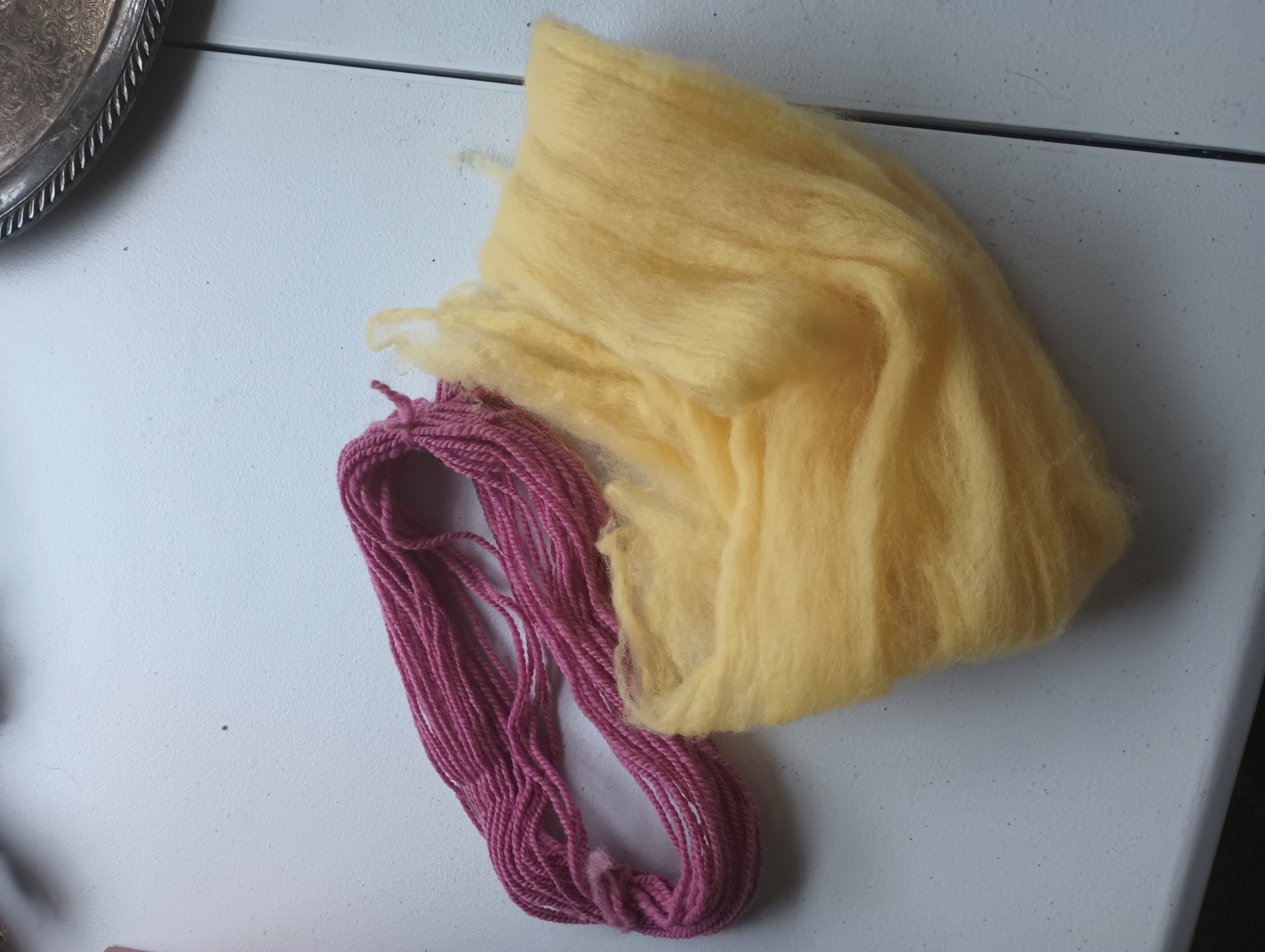 A small skein of magenta cochineal-dyed yarn sits next to a small amount of yellow osage-dyed roving.
