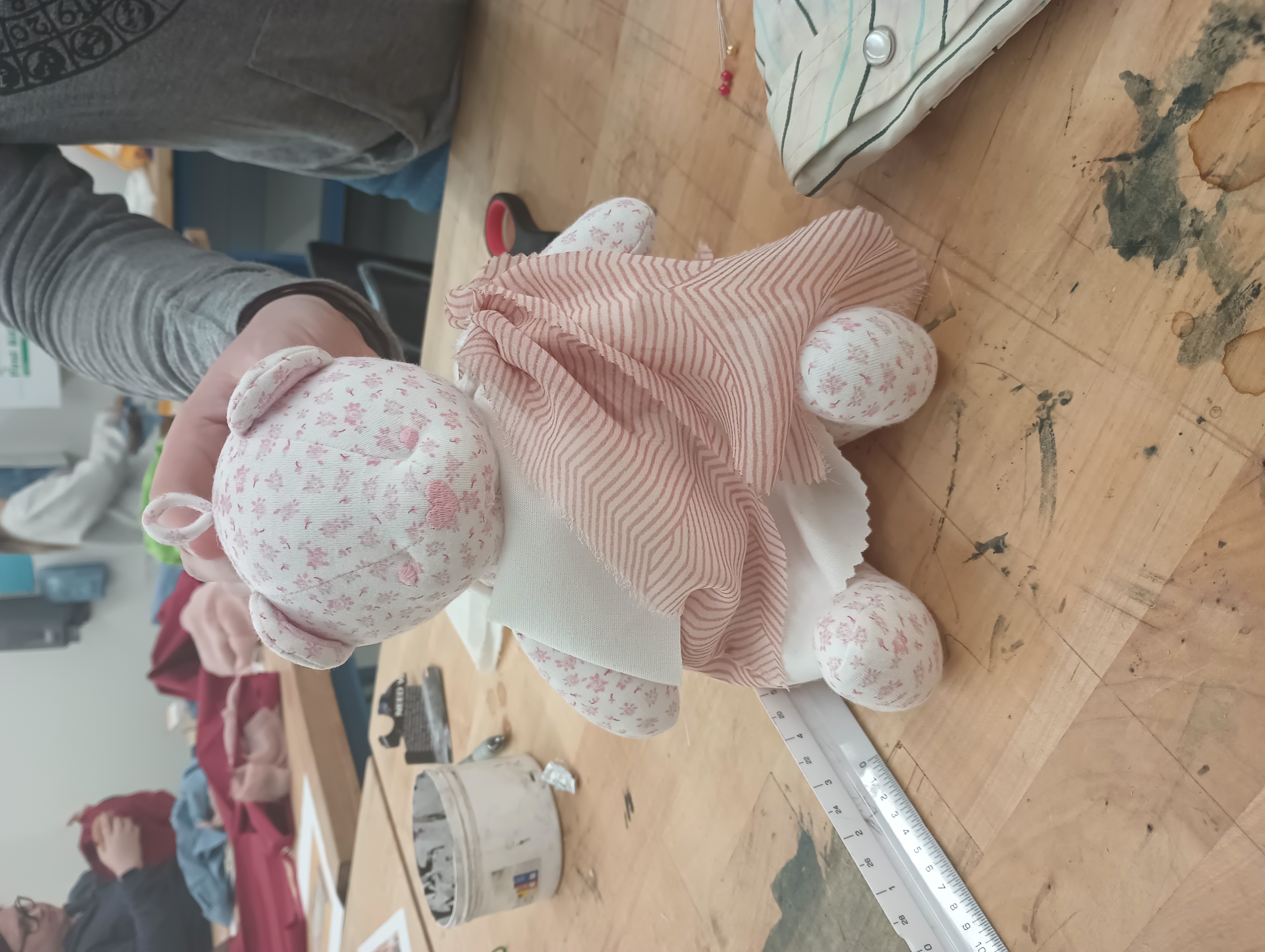 A small pink and white teddy bear wearing a mini white peplos and a sheer pink himation.