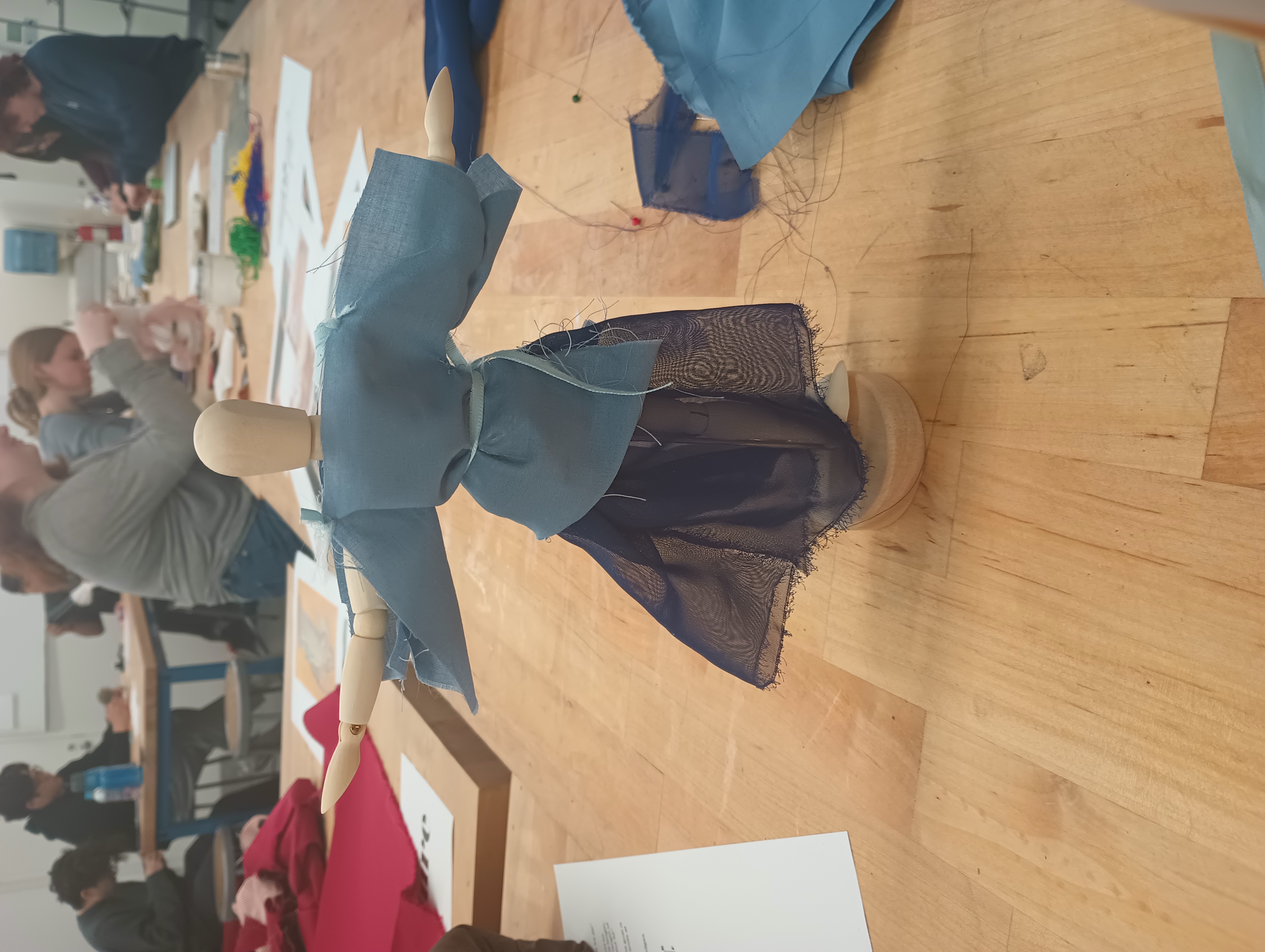 A small art mannequin wearing a sheer gathered dark blue skirt and a simple pale blue top with open sleeves.