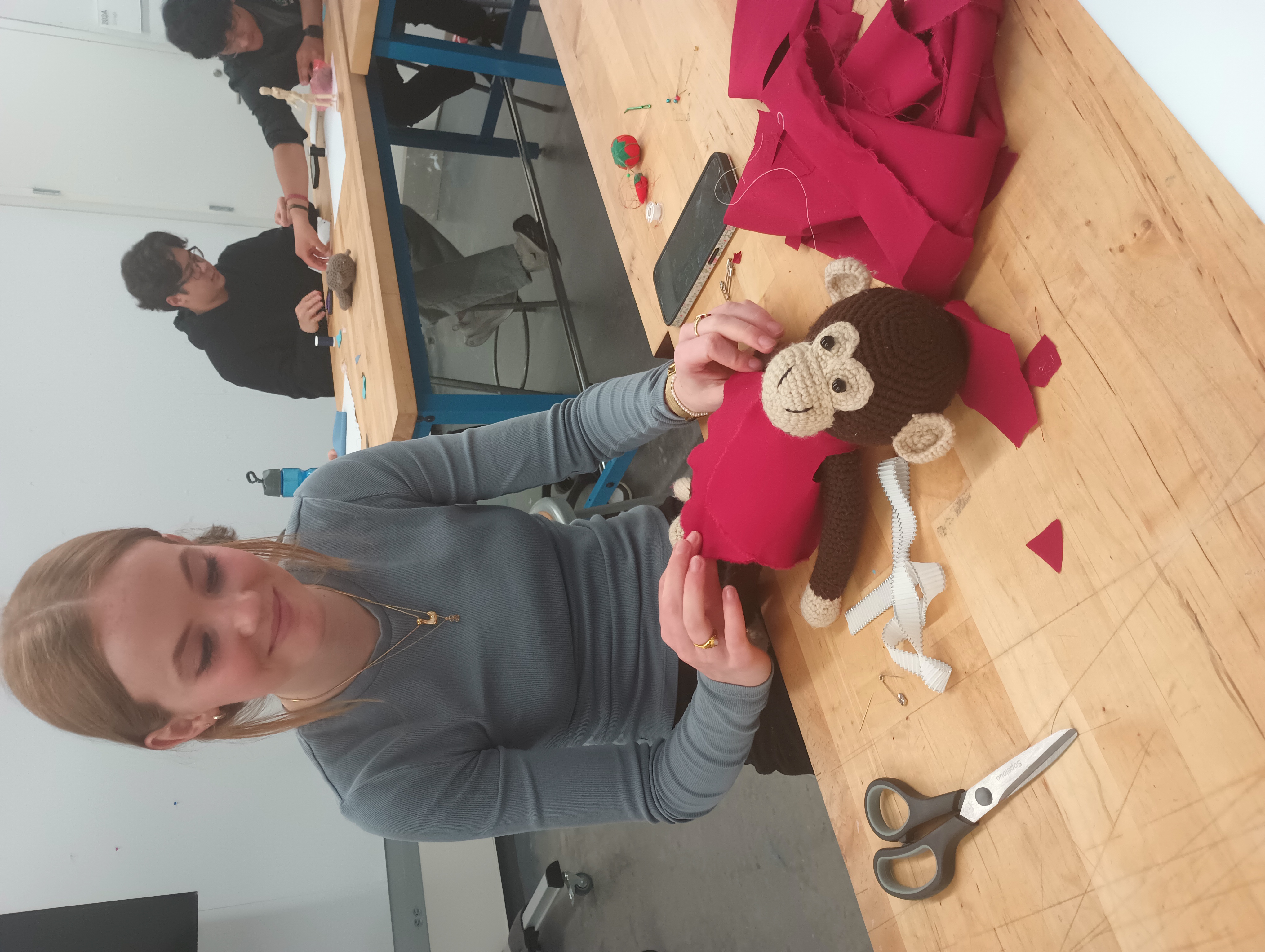 A student fits a red tunic onto a stuffed monkey.