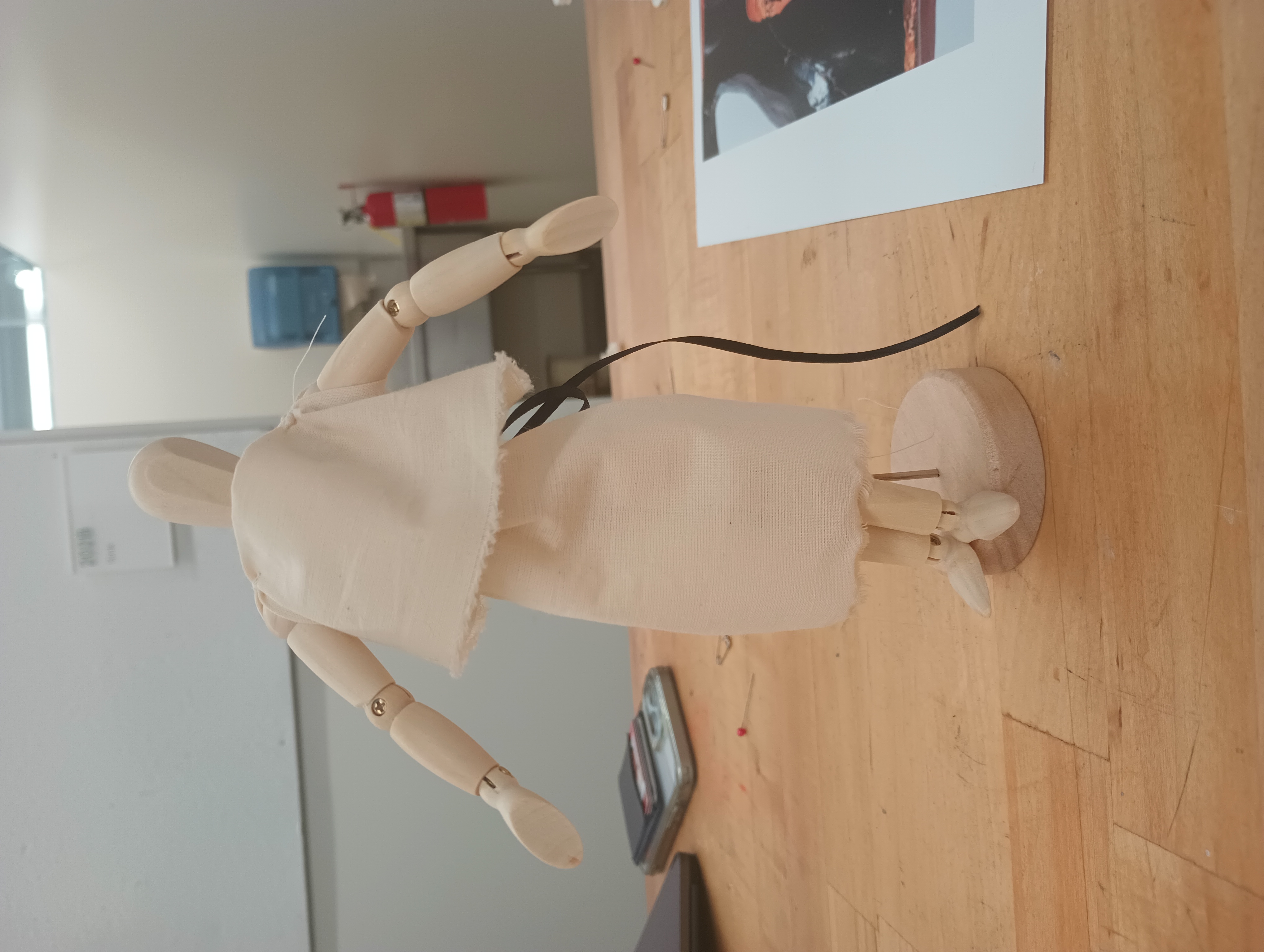 A small art mannequin wearing a white peplos belted with a black ribbon.