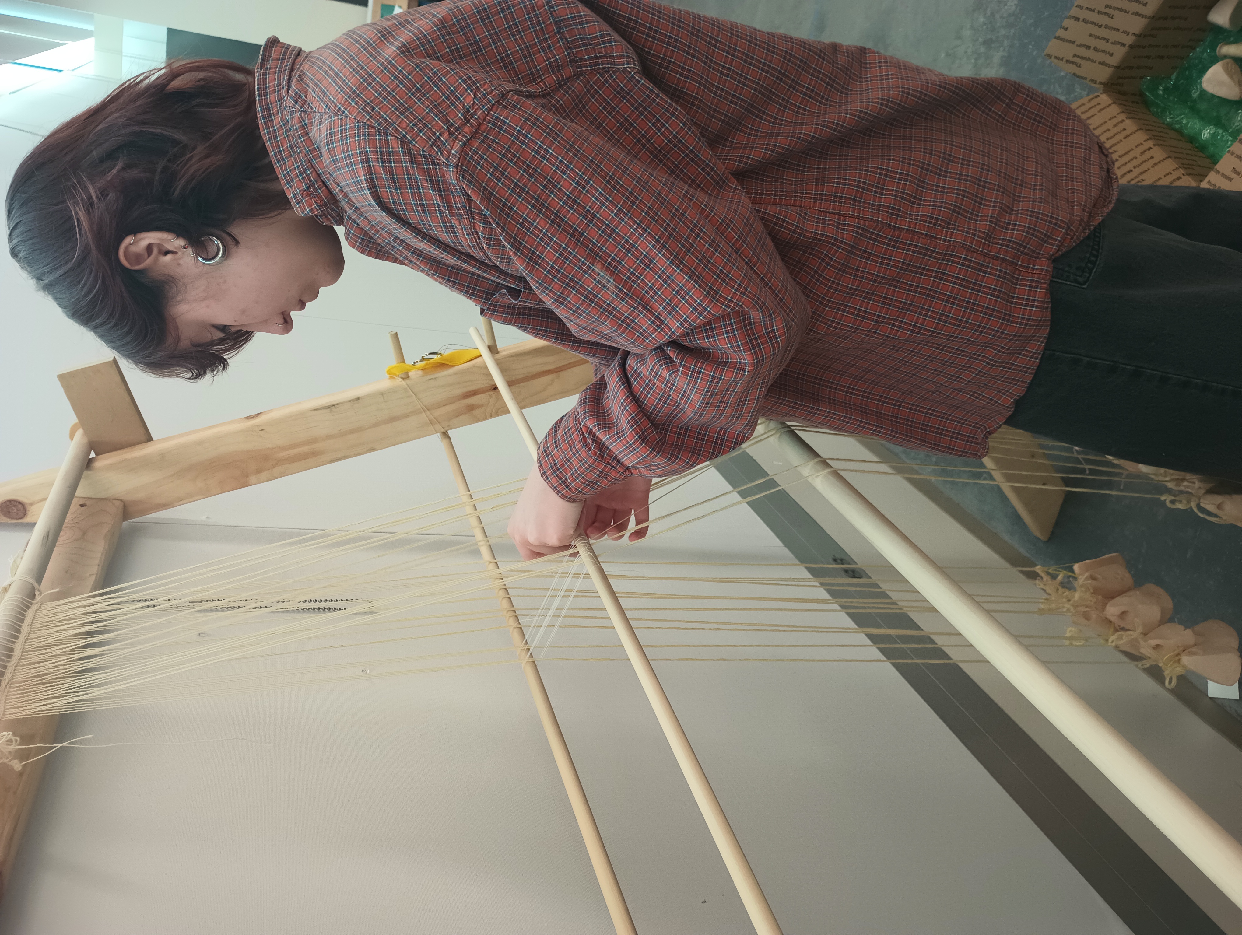 A student knits string heddles around the warp threads attached to the warp-weighted loom. This is a process that is quite difficult to explain in words if you aren't already familiar with it.