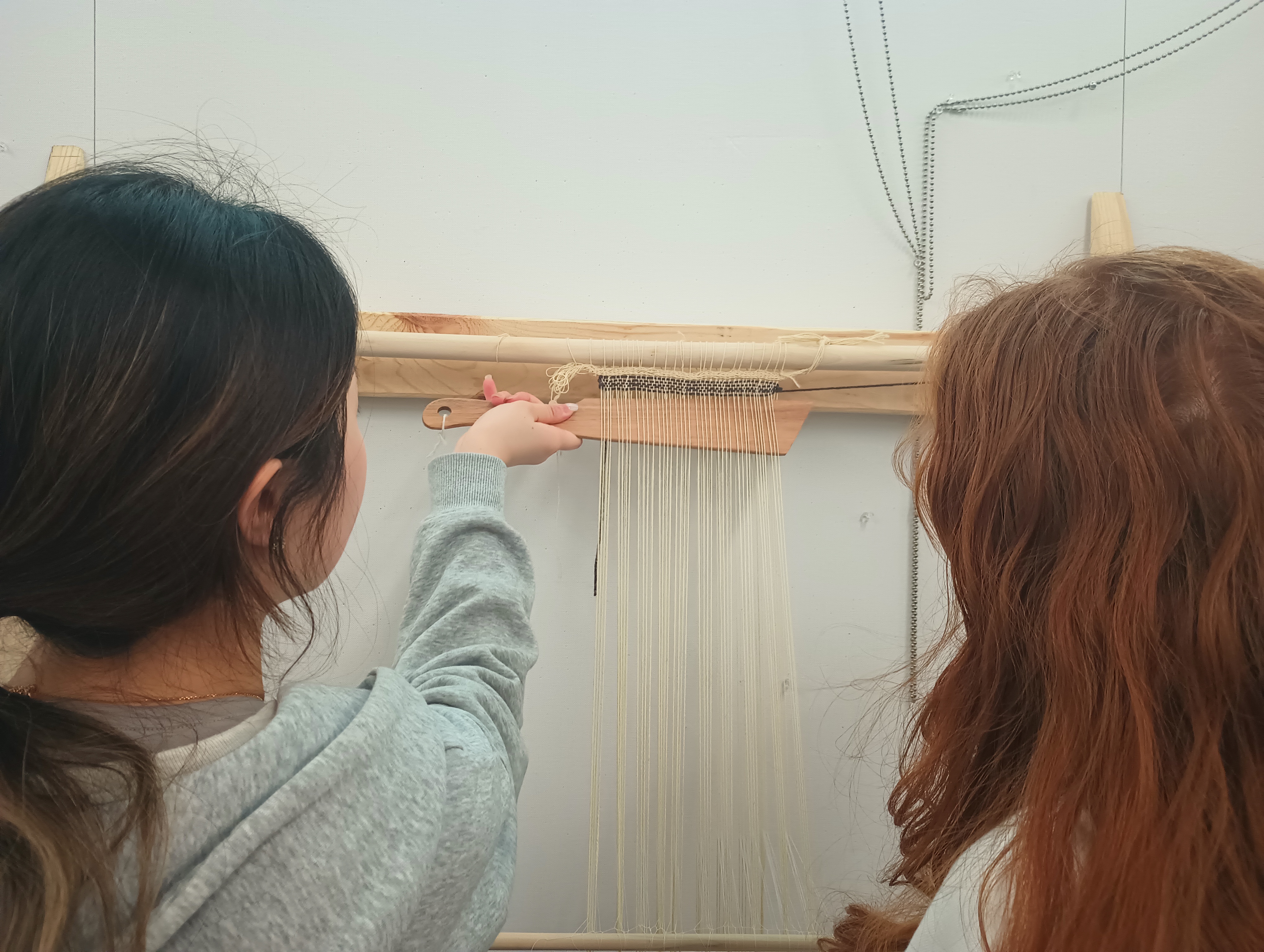 A student beats a weft thread upwards into the woven fabric using a weaving sword. The weaving sword is a wooden implement shaped like a short sword inserted into the warp. The edge is used to push the new weft thread upwards.